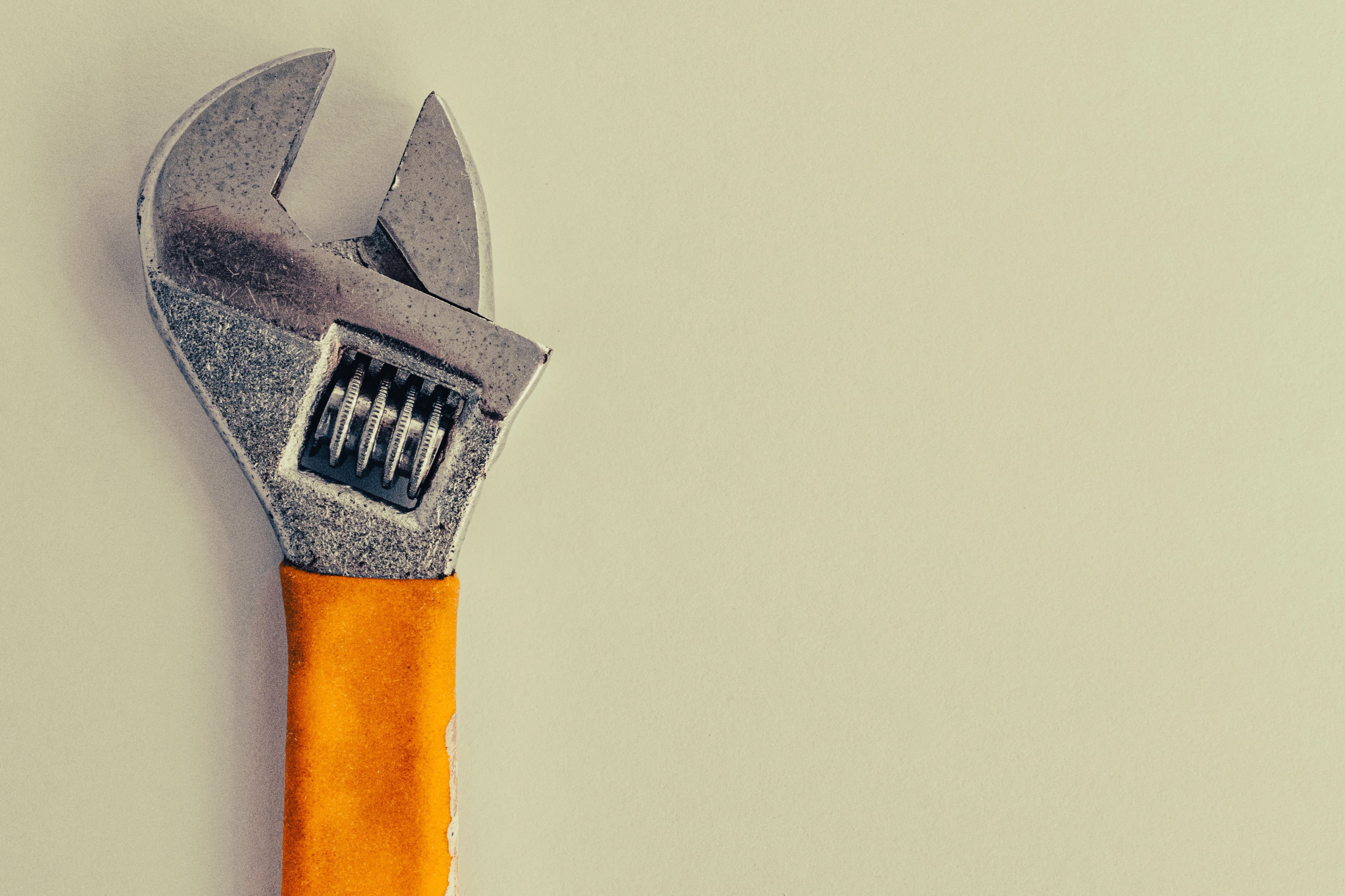 An adjustable wrench with an orange handle resting on a plain beige background.