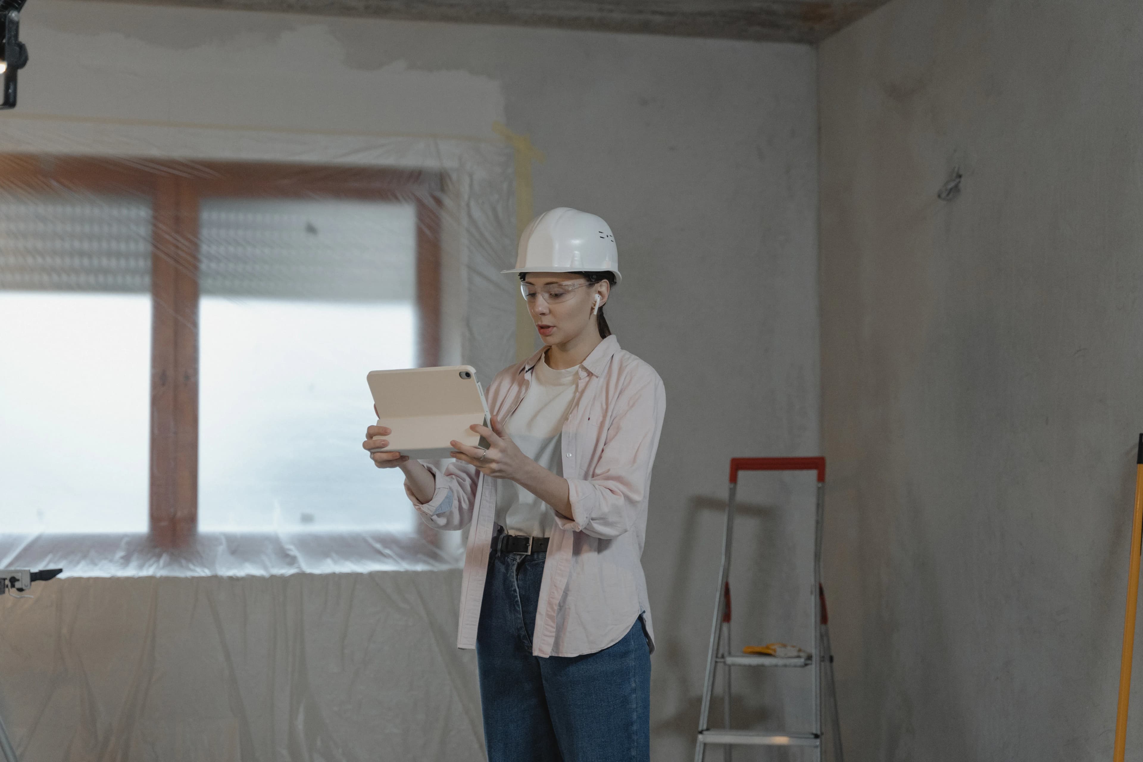 A contractor in a hard hat reviewing a tablet at a construction site.