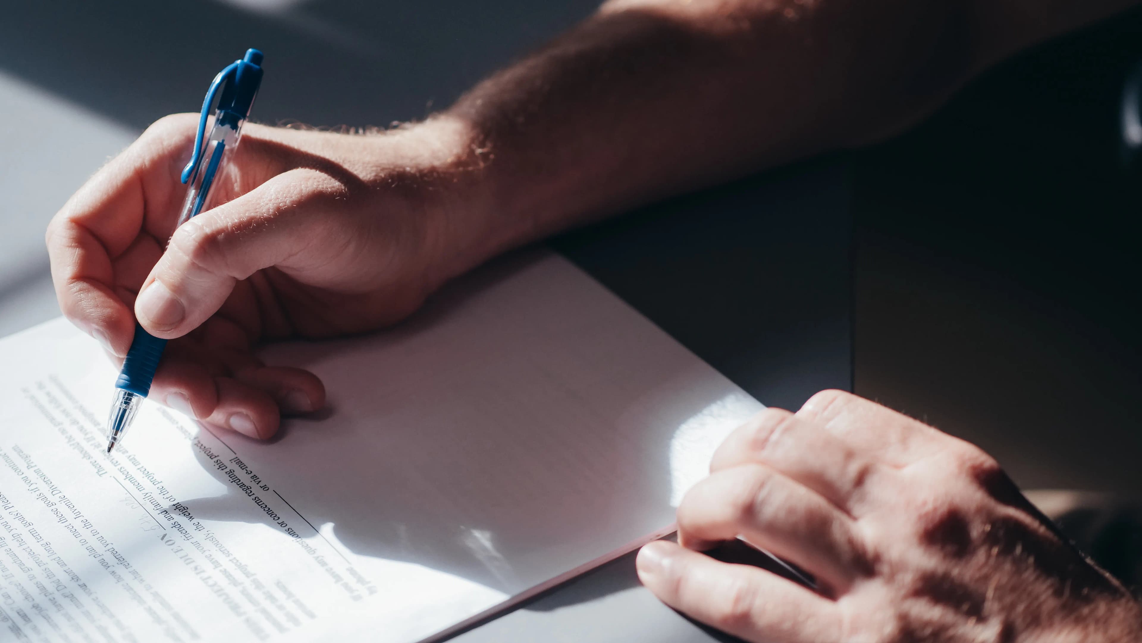 A person's hands signing a document with a blue pen.