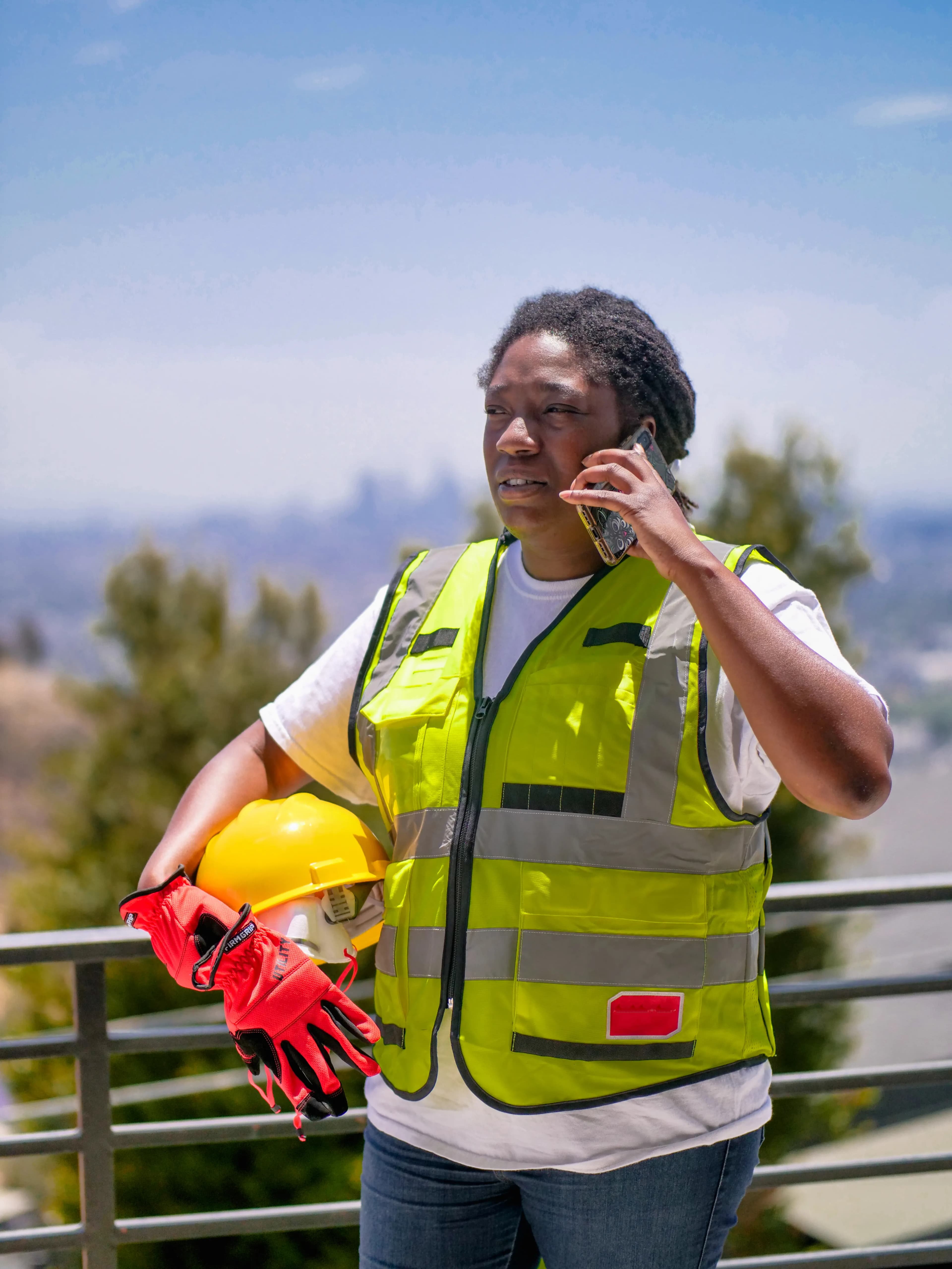 A construction worker in a safety vest taking a phone call on site.