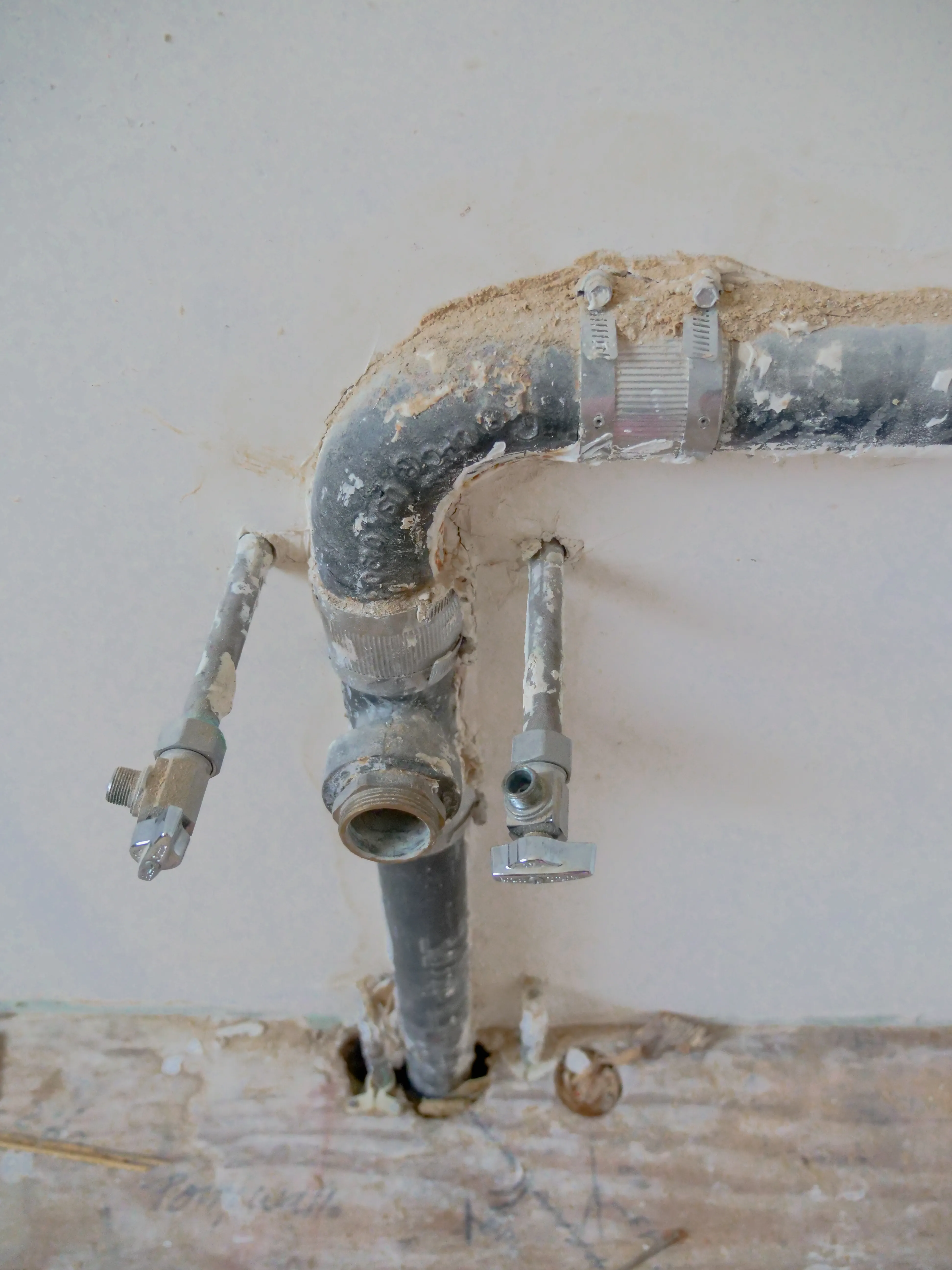A close-up of exposed plumbing pipes and shut-off valves on a wall.
