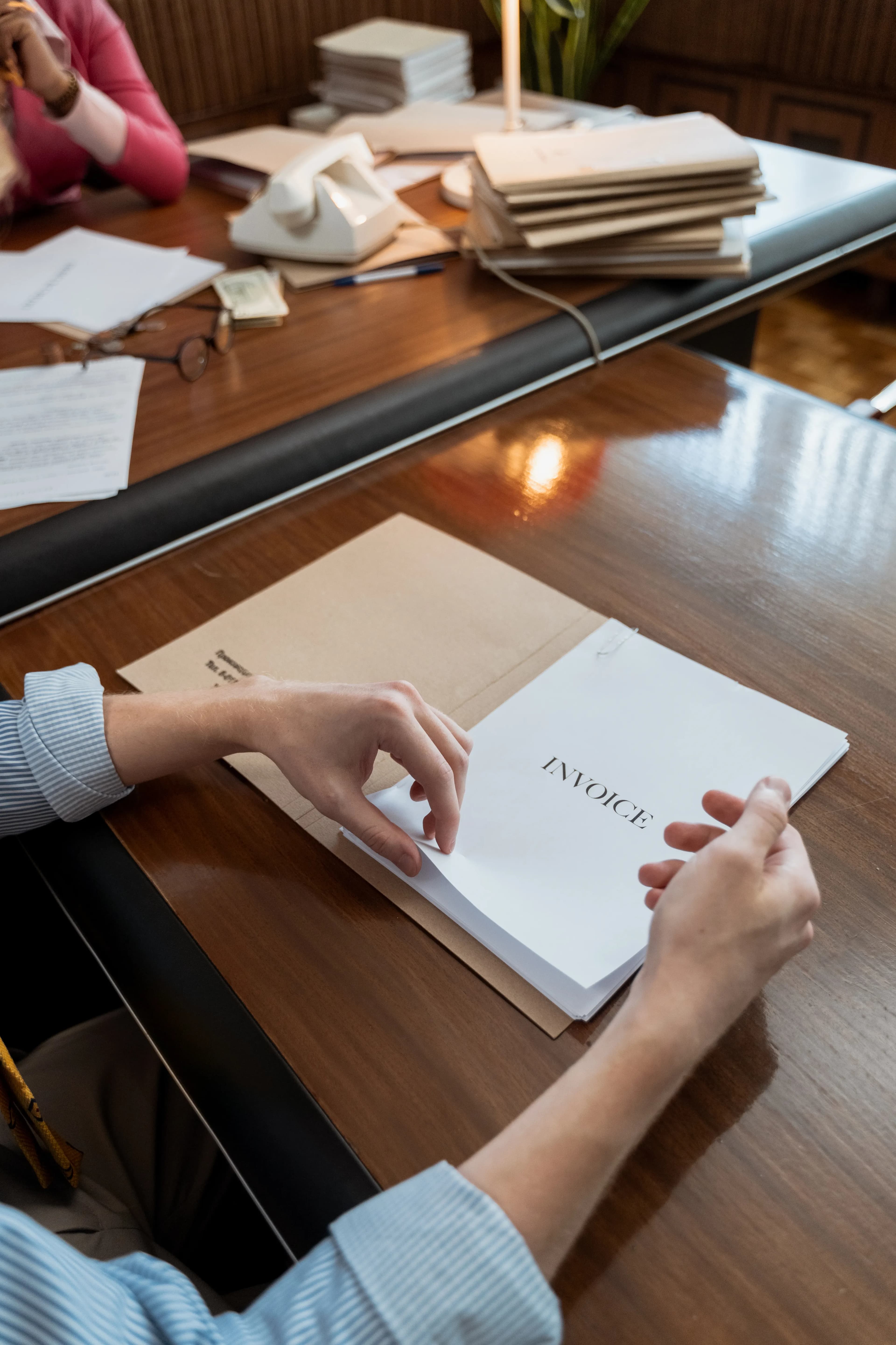 A person holding an invoice document on an office desk.